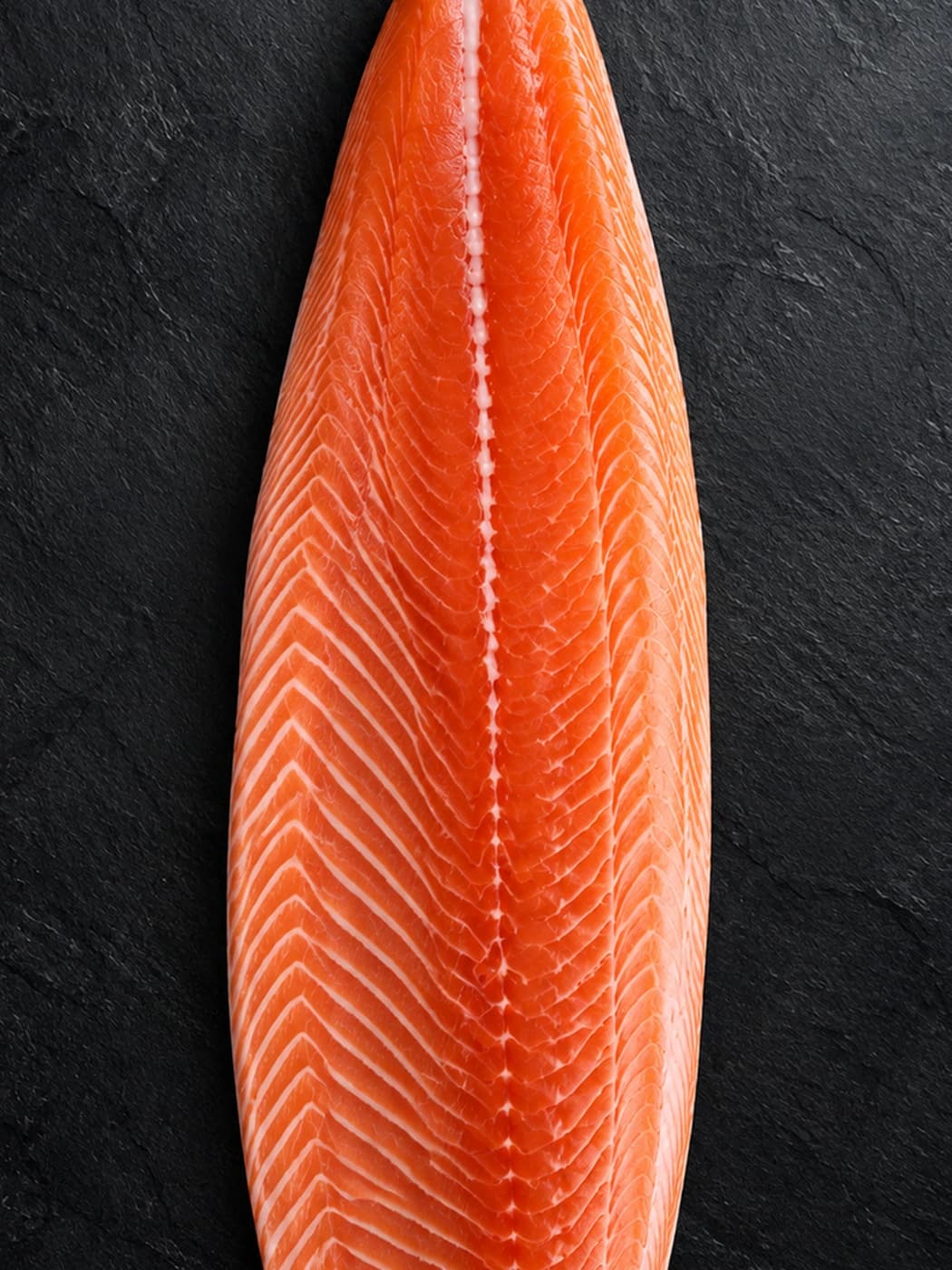 Ein ganzes Atlantiklachsfilet, von oben auf dunklem Schiefer fotografiert